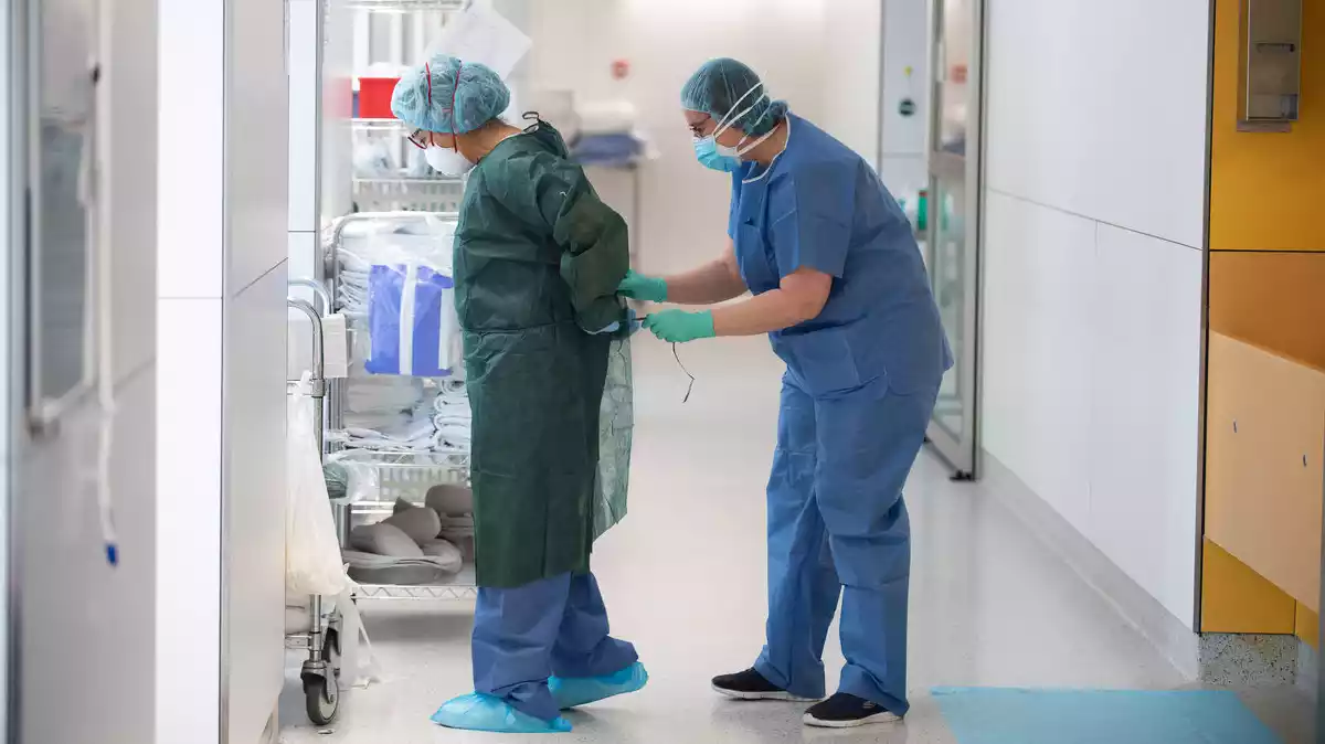 Una professional sanitària corda a una companya una bata abans d'atendre un pacient amb Covid-19
