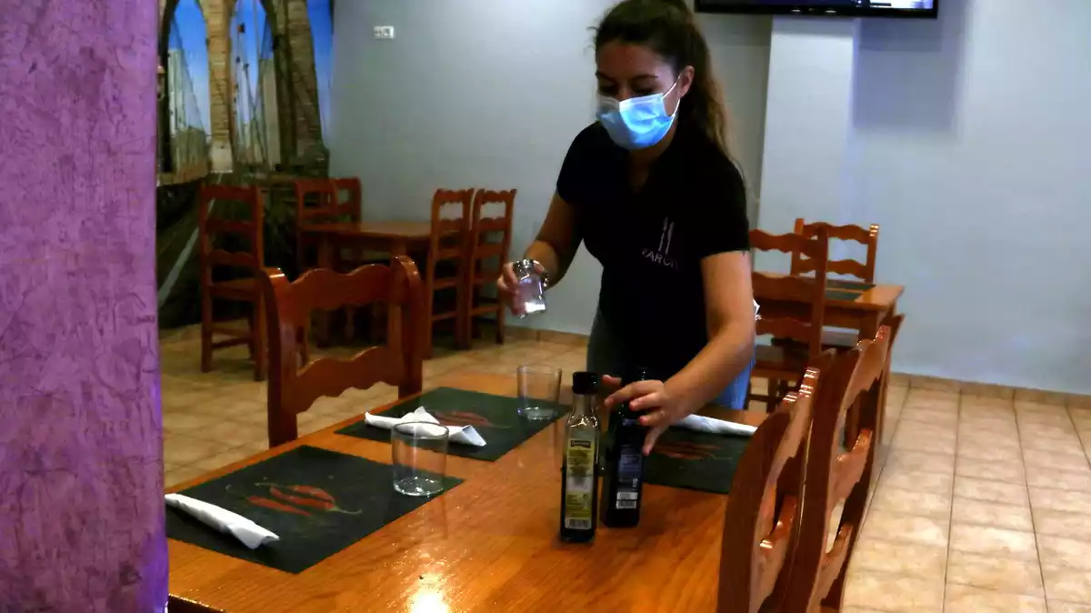 Pla mitjà de la cambrera del bar restaurant Farcit de Tortosa posant setrilleres a les taules per rebre els clients per dinar.