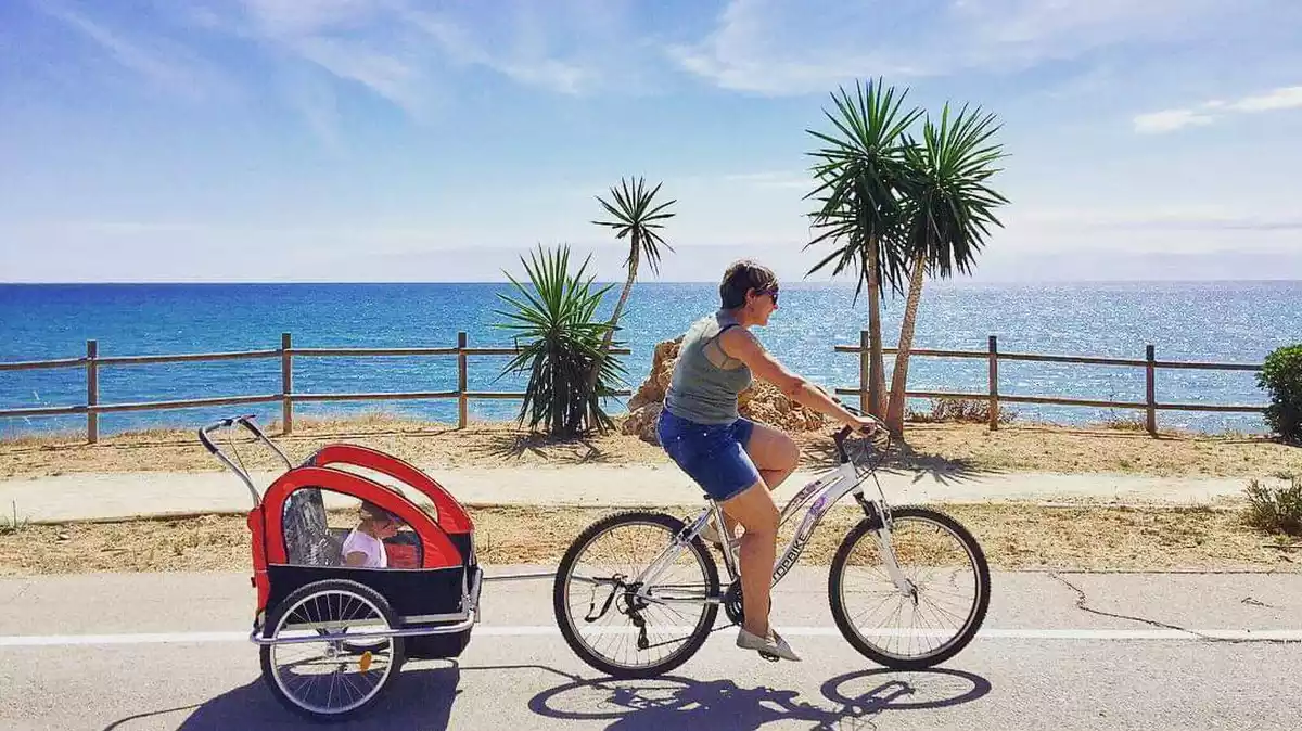 Una dona amb bicicleta passejant un infant al municipi d'Alcanar