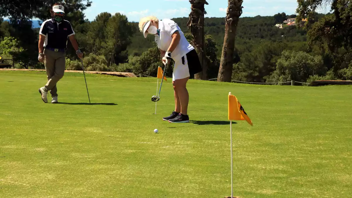 Una dona rebent una classe de golf al Golf Costa Daurada, a Tarragona, amb el professor distanciat i tots dos amb mascareta.