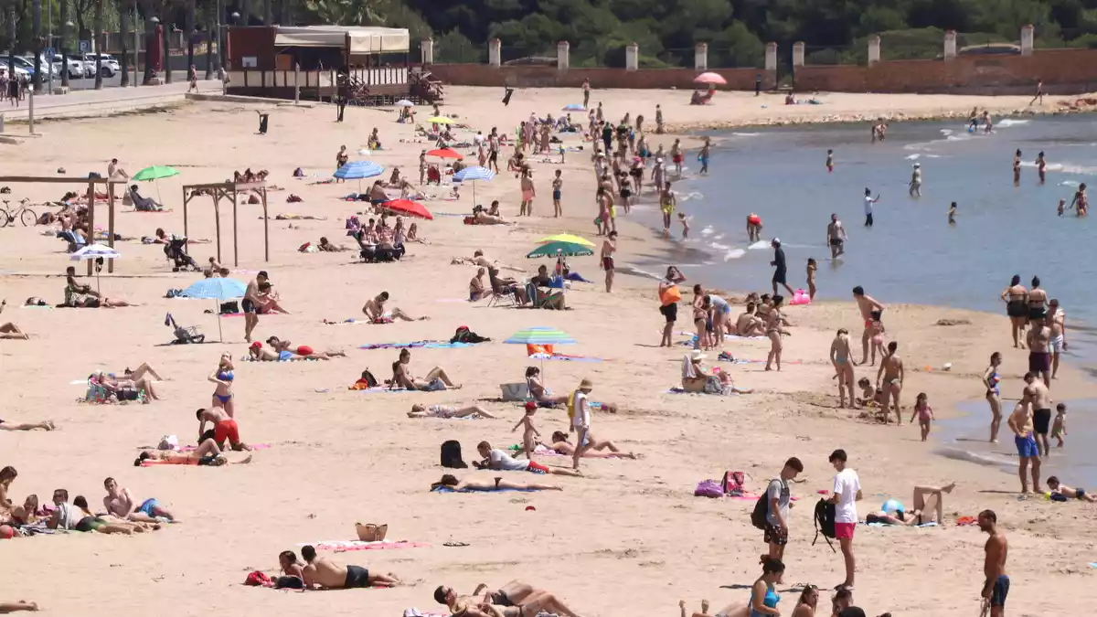 Pla mitjà de la platja de l'Arrabassada de Tarragona, amb banyistes i gent prenent el sol.