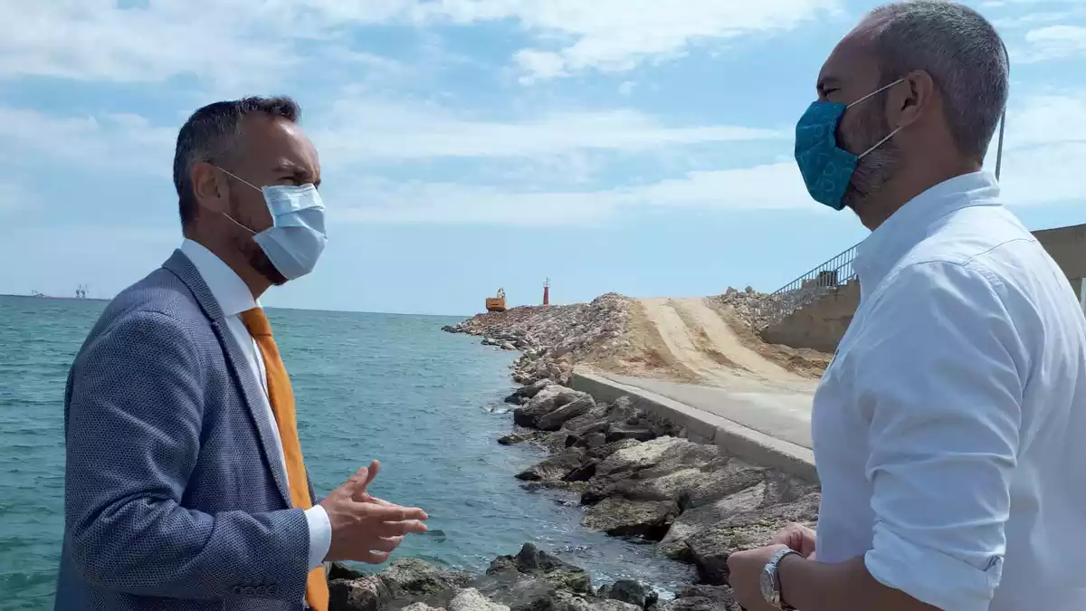 Pla mitjà del director general de Ports, Joan Pere Gómez, i l'alcalde d'Alcanar, Joan Roig, conversant al port de Les Cases amb les obres en marxa de fons.