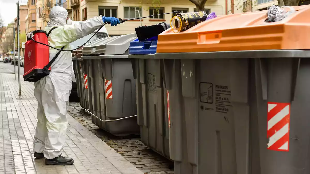 Un operari del servei de neteja viària de Reus desinfecta una illa de contenidors, alguns dels quals són plens