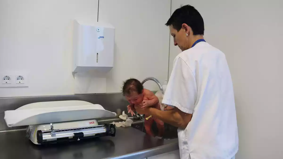 Una infermera pesant i mesurant un nadó acabat de néixer