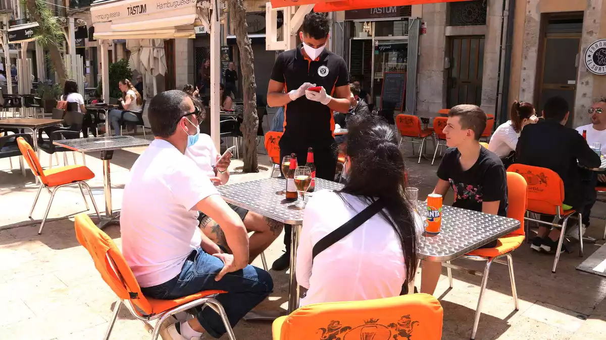 Pla obert d'un cambrer anotant la comada a uns clients en una terrassa de la plaça de la Font de Tarragona en el primer dissabte de la fase 1.