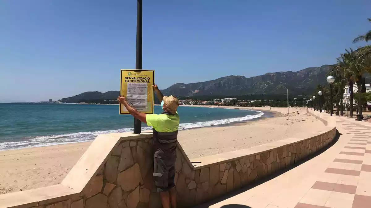 Pla general d'un operari de l'Ajuntament de Vandellòs i l'Hospitalet de l'Infant col·locant un cartell informatiu en una de les platges del municipi.