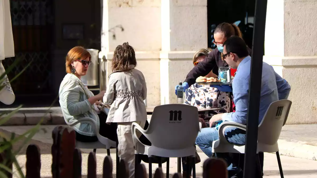 Pla general d'una família asseguts a la terrassa d'un bar a Tortosa on els serveixen l'esmorzar.