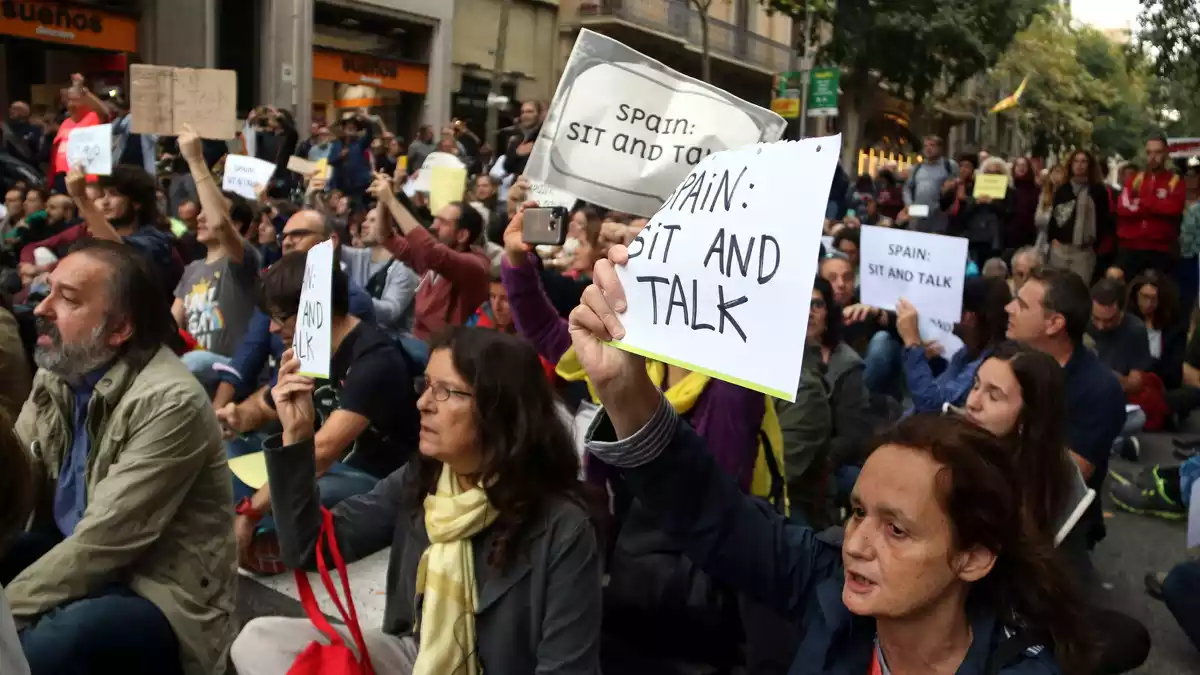 Manifestants asseguts davant la Delegació del govern espanyol amb cartells de 'Sit and Talk' el 21 d'octubre de 2019