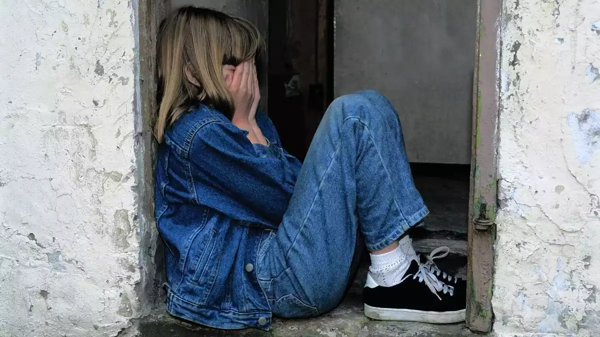 Imatge d'arxiu d'una nena asseguda a terra tapant-se la cara